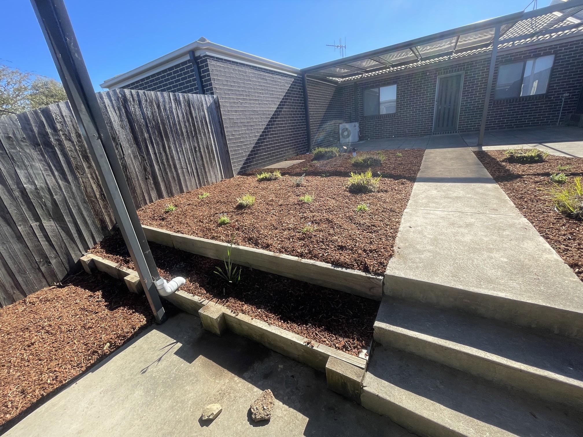 A gardener spreading wood chip mulch evenly across a garden bed with a rake.